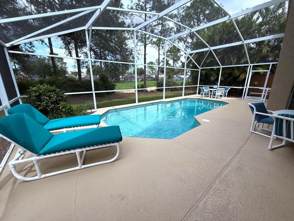 A covered outdoor swimming pool with lounge chairs and a view of the surrounding greenery. - Liquid Sunshine Villa (Haines City)