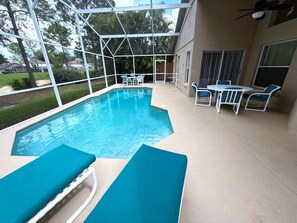 A swimming pool with lounge chairs and a table, surrounded by a covered patio area. - Liquid Sunshine Villa (Haines City)