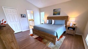 A bedroom with a wooden bed, a nightstand, a lamp, and a painting on the wall. - Prestige on the Fairway (Haines City)