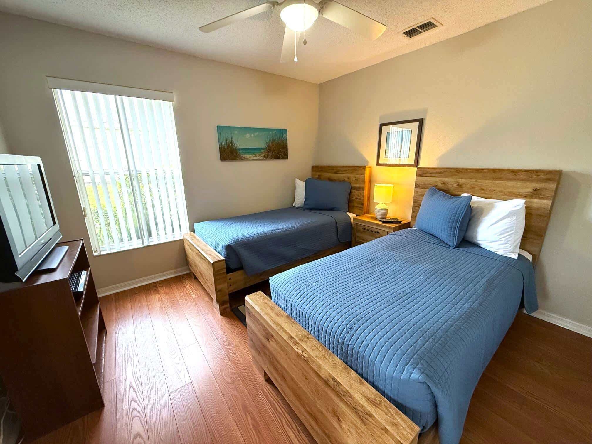 A bedroom with two beds, a TV, and a ceiling fan.