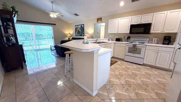 A modern kitchen with white cabinets, a central island, and a large window. - Prestige on the Fairway (Haines City)