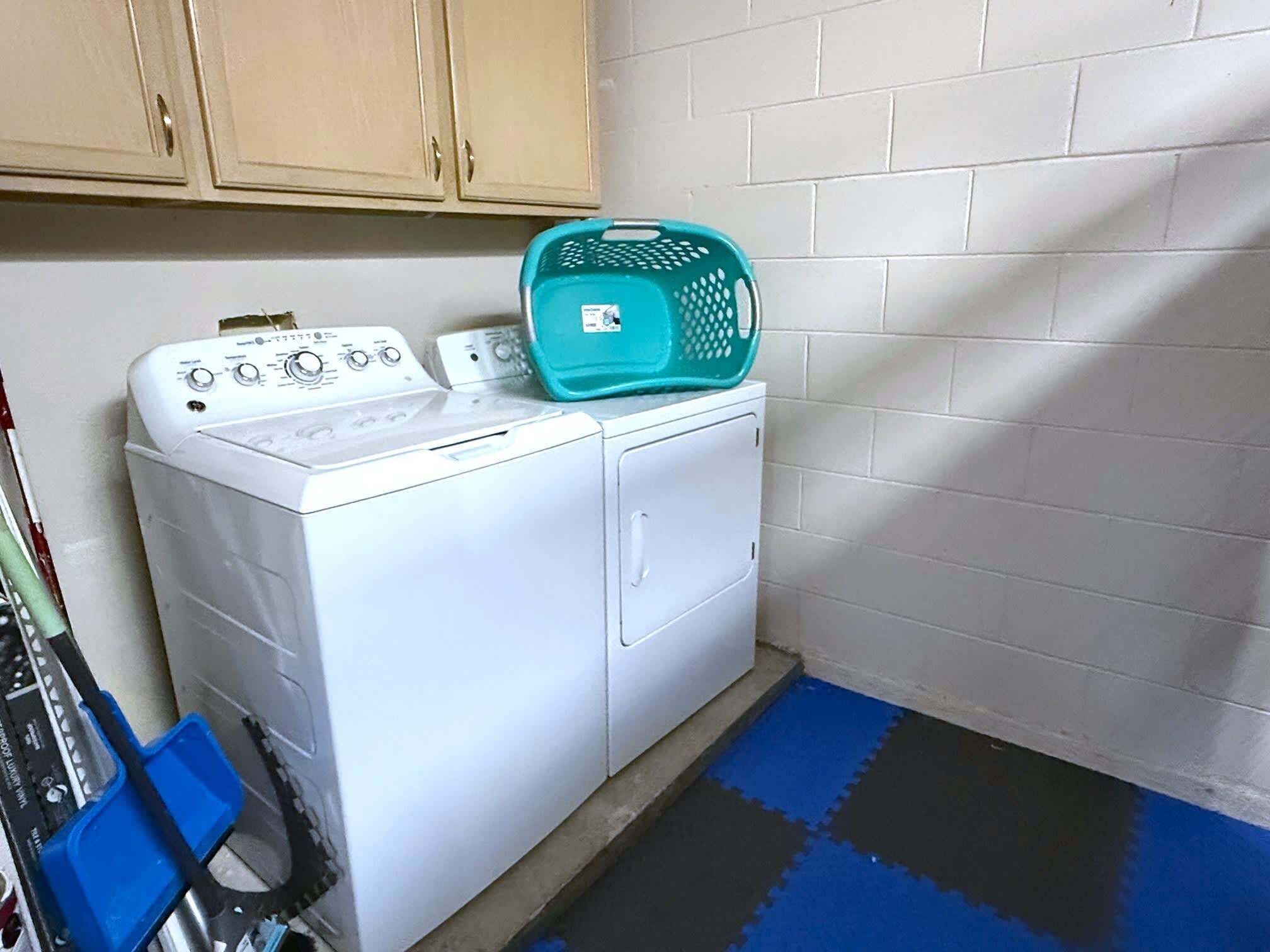 A laundry area with a washing machine, a blue laundry basket, and a blue and black floor mat.