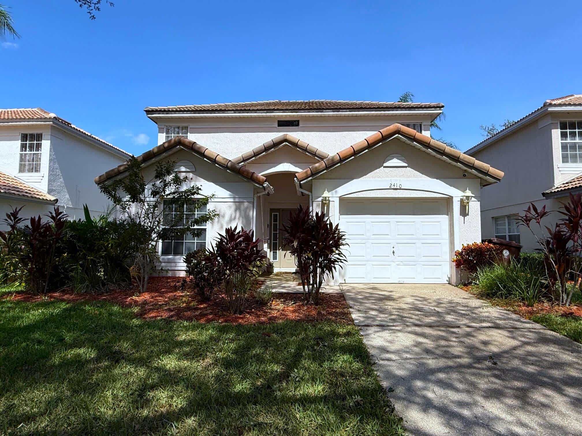 A two-story house with a white exterior, a garage, and a well-maintained lawn with various plants.