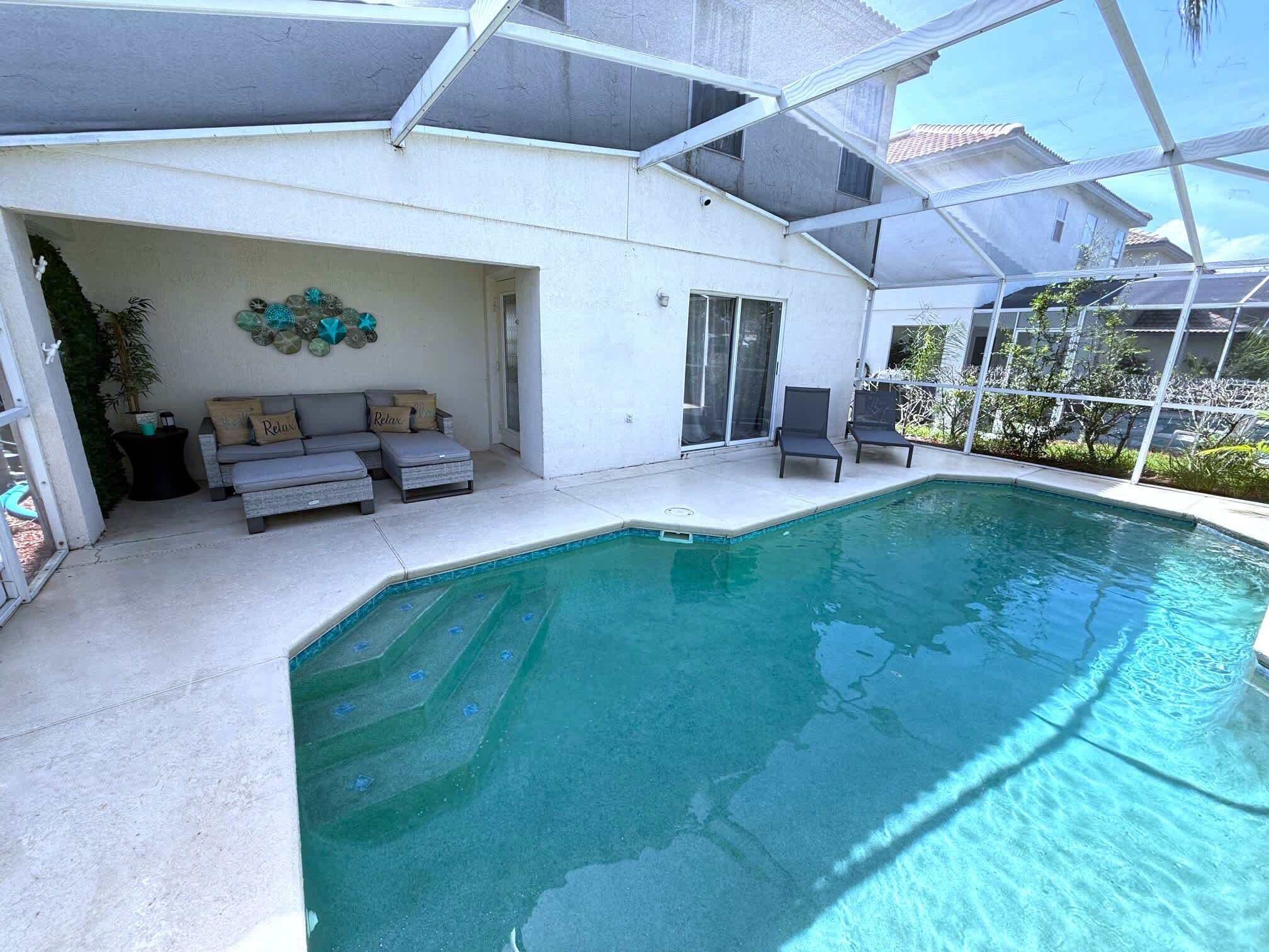 A pool area with a covered patio, a sofa, and a small table.