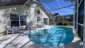 A pool area with a glass enclosure, lounge chairs, and a view of a house. - Pool Pixie Estate (Haines City)
