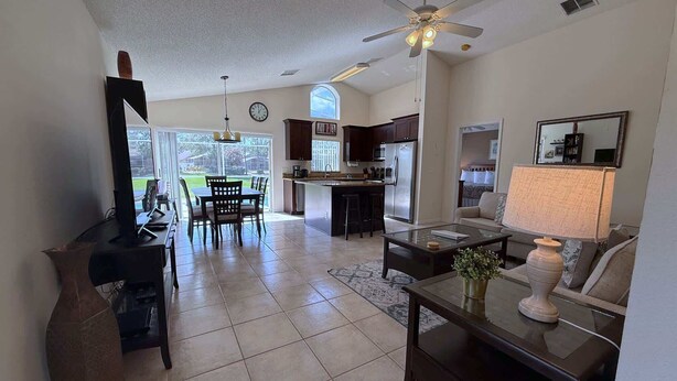A spacious living area with a dining table, kitchen, and a ceiling fan. - Pool Pixie Estate (Haines City)