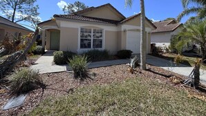 A residential house with a garage, a front yard with a palm tree, and a clear blue sky. - Pool Pixie Estate (Haines City)