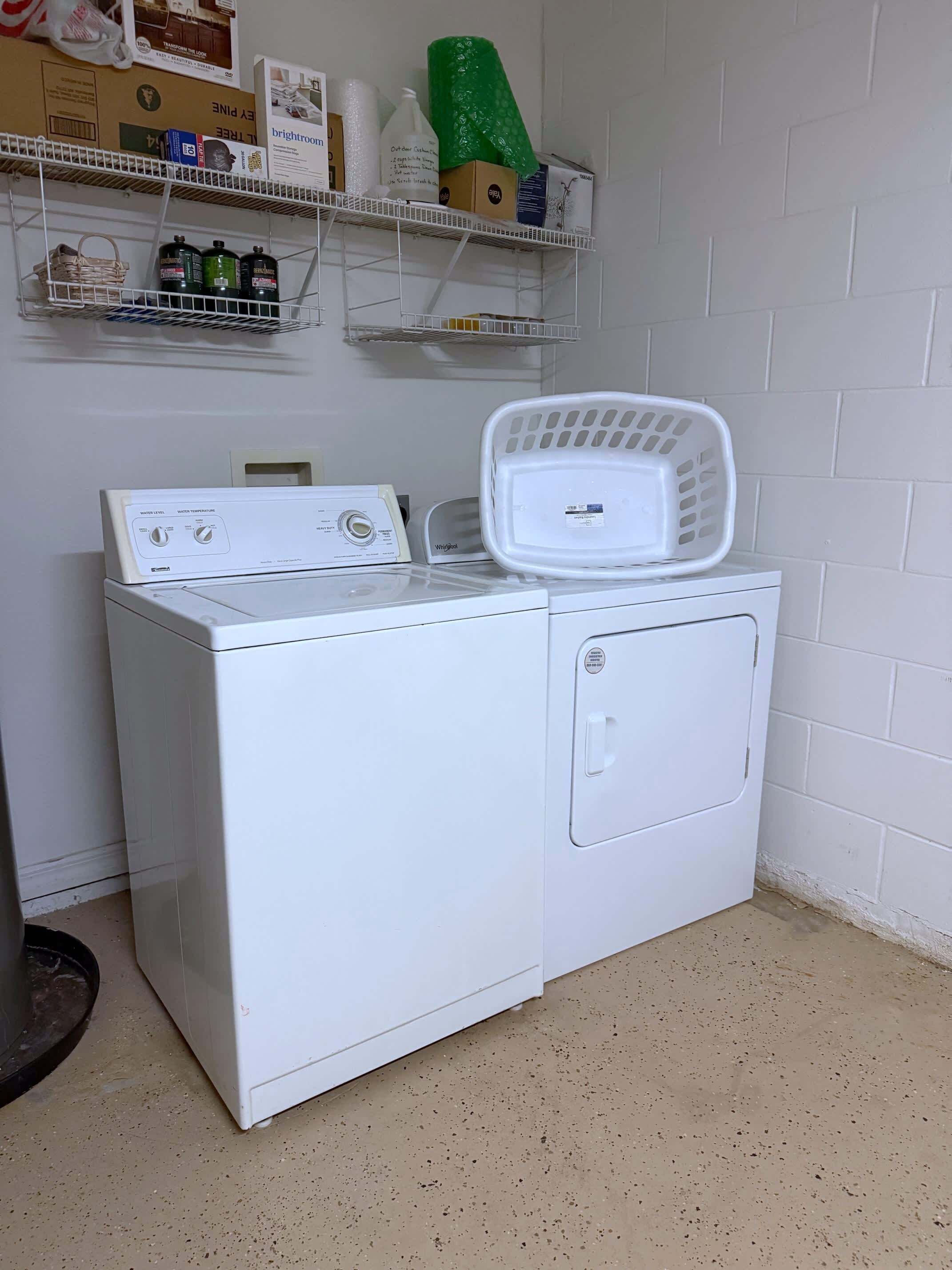 A front-loading washer and dryer in a laundry room with a shelf above containing various items.