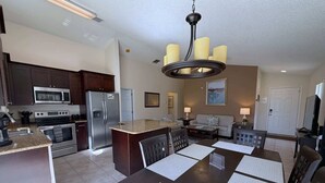 A modern kitchen with a central island, stainless steel appliances, and a dining area with a large table and chairs. - Pool Pixie Estate (Haines City)