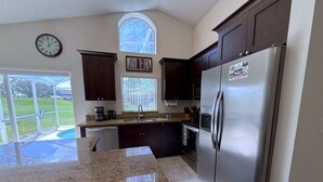 A kitchen with granite countertops, stainless steel appliances, and a window overlooking a backyard. - Pool Pixie Estate (Haines City)