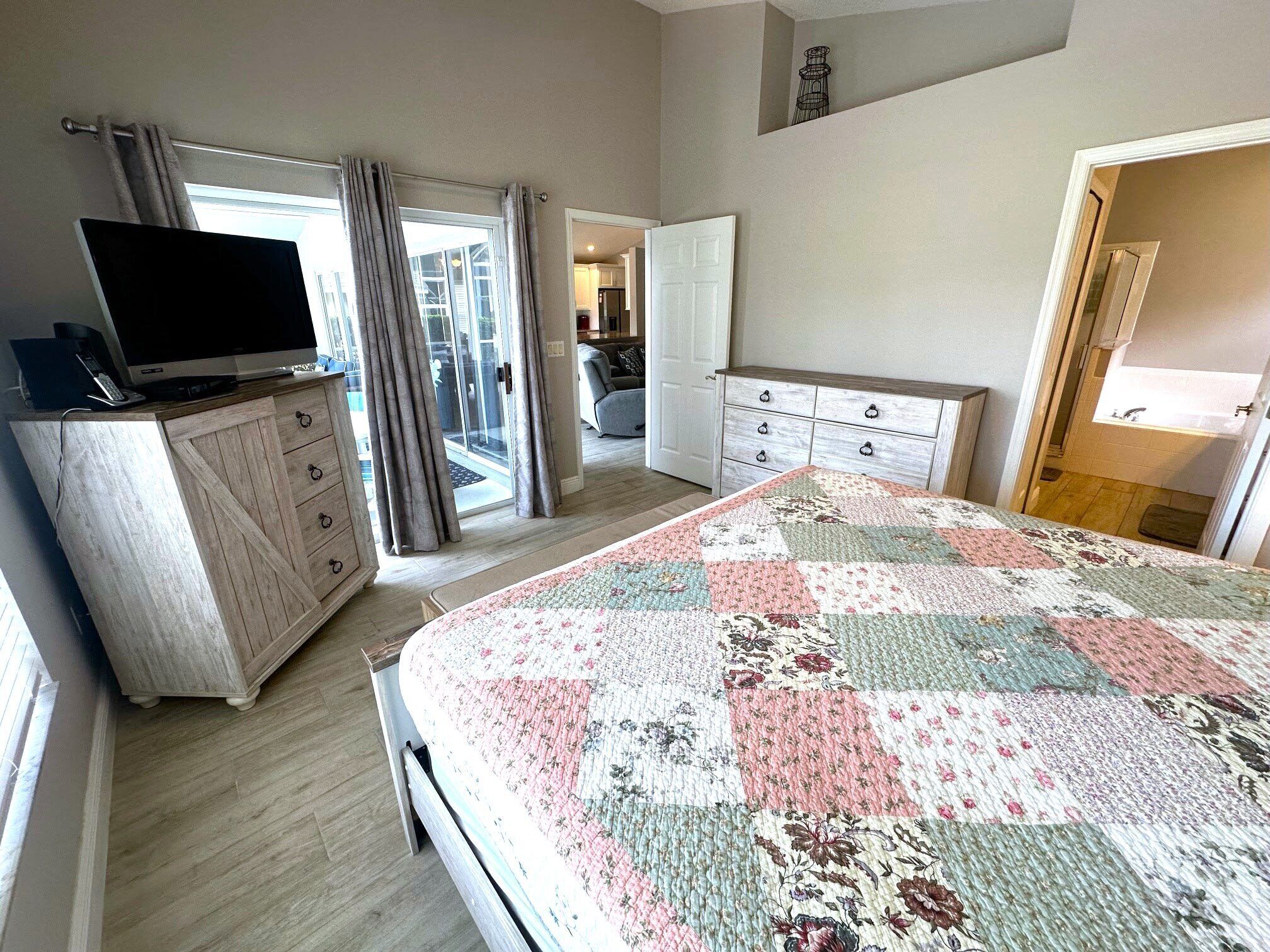 A bedroom with a bed, a TV on a dresser, a wardrobe, and a view of the outside.