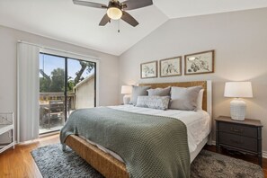 Un dormitorio con cama, mesitas de noche, ventilador de techo y vistas a través de un ventanal corredero.