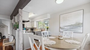 A modern kitchen with white cabinetry, a dining area with a round table and white chairs, and a large abstract painting on the wall. - 2625 Forest Ridge | Pool | Tennis/Pickleball | Large Deck (Fernandina Beach)