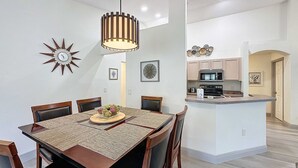 A modern kitchen with a central island, wooden dining table with chairs, and a hanging pendant light. - Eagle’s Nest Villa (Haines City)