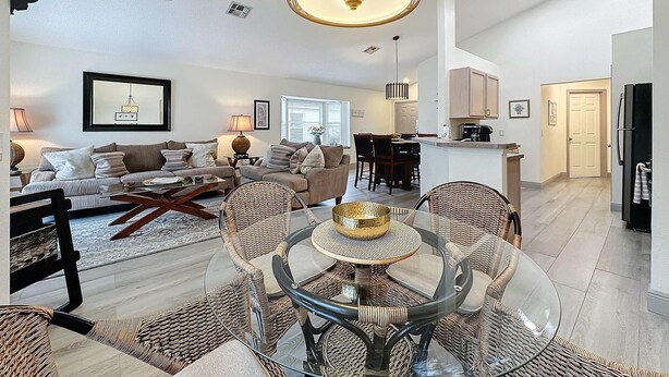 A spacious living room with a dining area, kitchen, and a large chandelier. - Eagle’s Nest Villa (Haines City)
