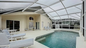 A covered outdoor swimming pool with lounge chairs and a patio area. - Eagle’s Nest Villa (Haines City)
