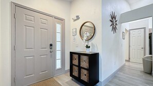 A hallway with a grey door, a black console table with a mirror, and a decorative star on the wall. - Eagle’s Nest Villa (Haines City)