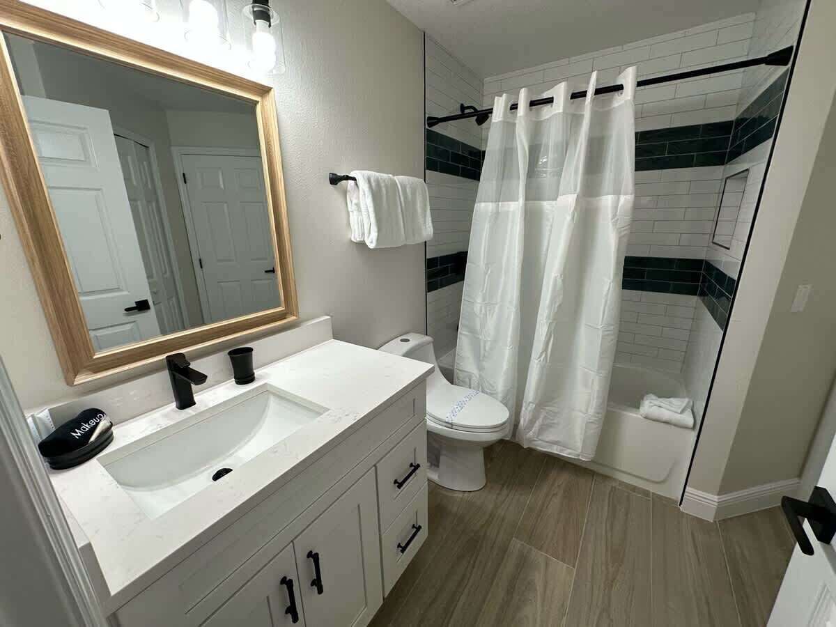 Ein modernes Badezimmer mit Waschbecken in Weiß, einem schwarzen Wasserhahn und einem großen Spiegel.