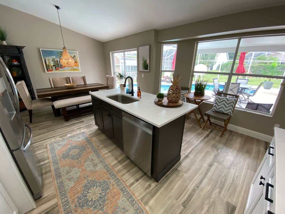 A modern kitchen with a central island, a dining area with a bench, and large windows offering a view of the outdoors.