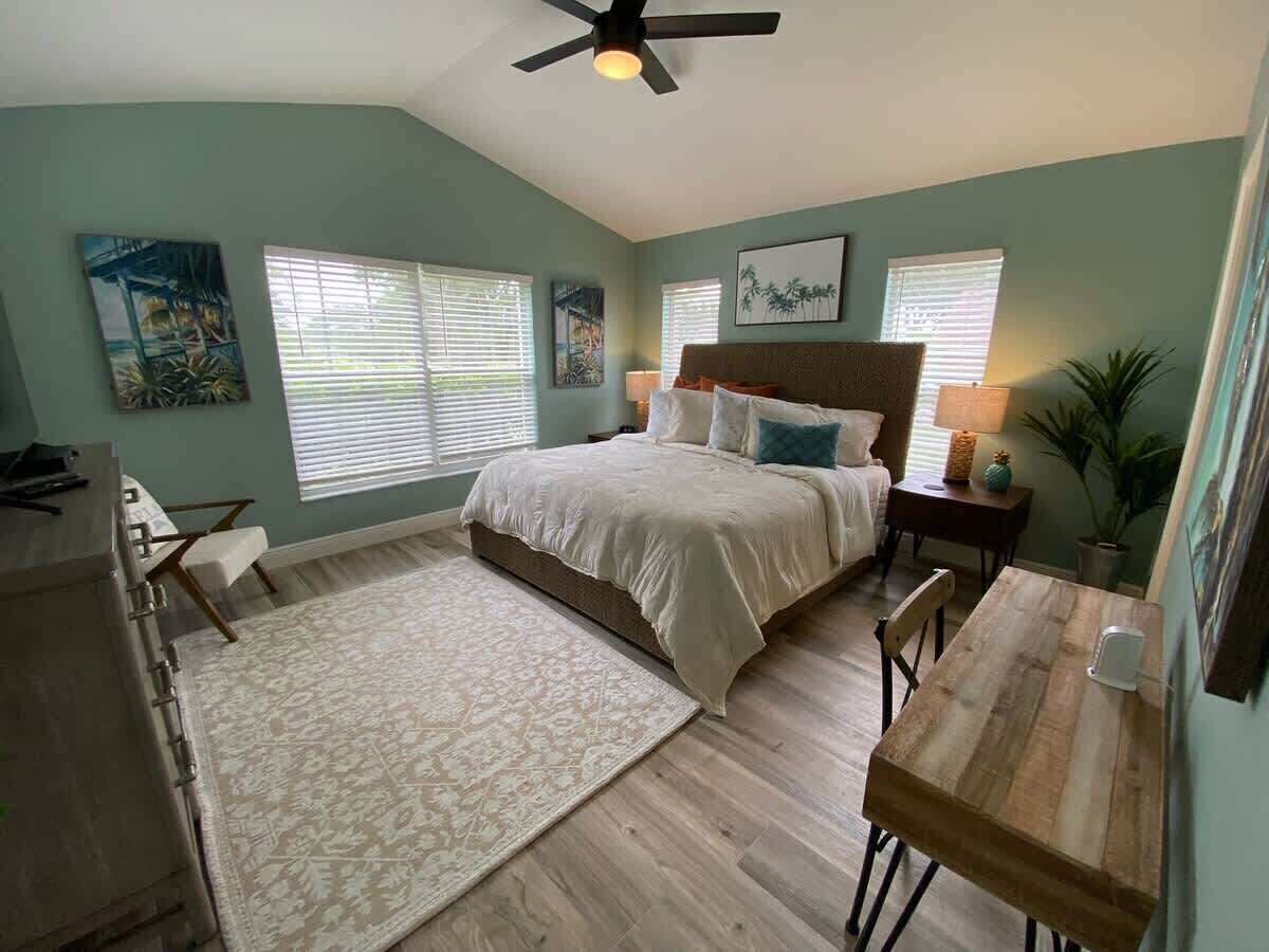 Une chambre à coucher comprenant un lit, un bureau, une chaise, une fenêtre et un ventilateur de plafond.