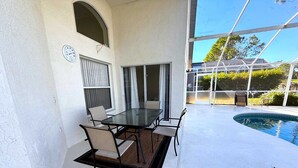 Une terrasse couverte avec une table et des chaises en verre, une piscine et une vue sur les environs.