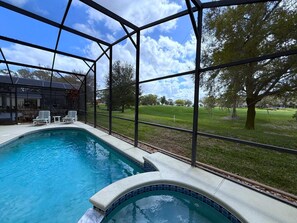 Une piscine dotée d’une enceinte en verre, entourée d’une pelouse et d’arbres.