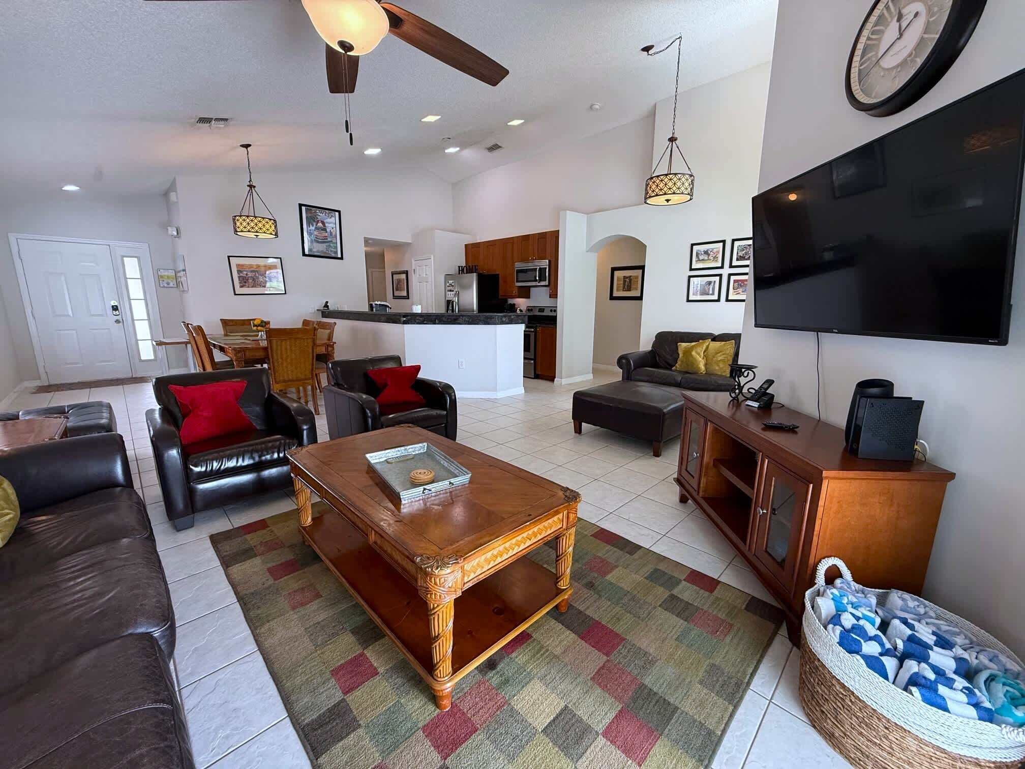 A spacious living room with a sofa, coffee table, and a TV. There is a kitchen area in the background.