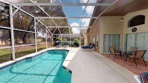 A covered outdoor swimming pool with lounge chairs and a patio table. - Oasis of Southern Dunes (Haines City)