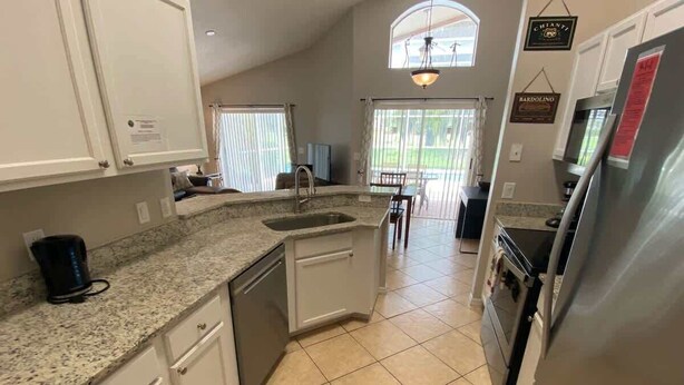 A kitchen with white cabinets, granite countertops, a stainless steel refrigerator, and a dishwasher. - Oasis of Southern Dunes (Haines City)