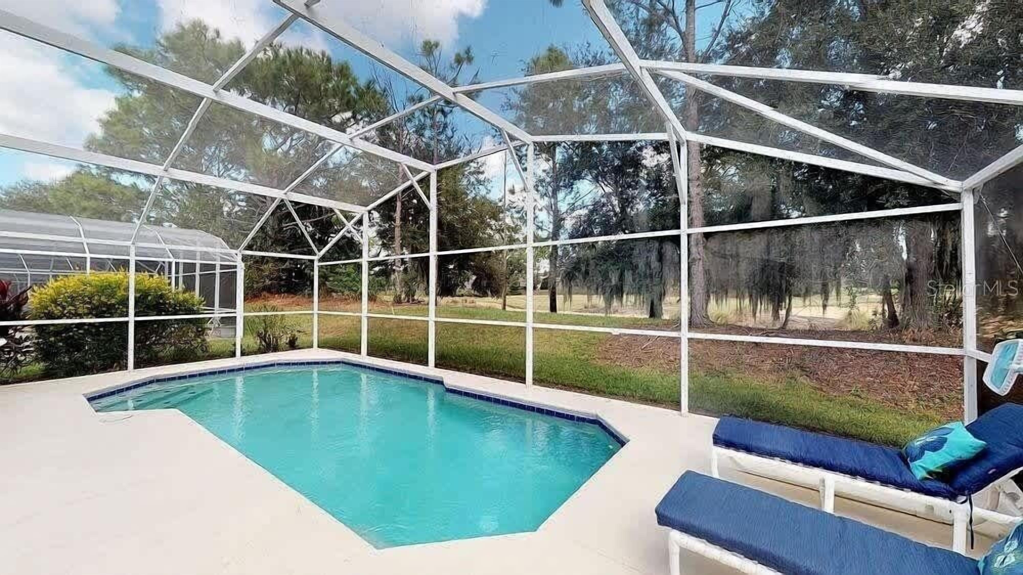 Un espace piscine doté d’une structure en verre, entouré de verdure et d’arbres.