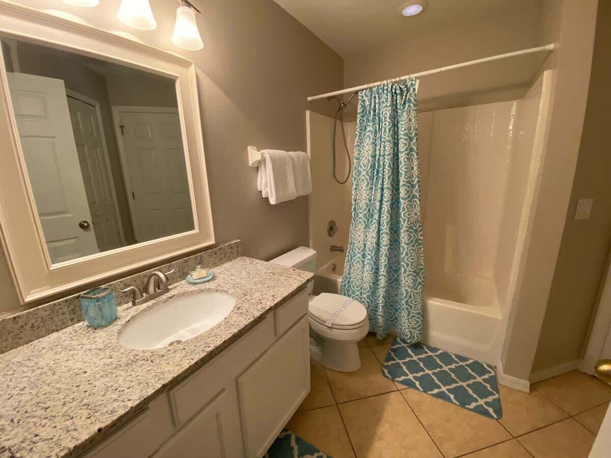A bathroom with a sink, mirror, toilet, shower, and patterned shower curtain.