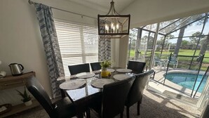 A dining area with a table set for four, surrounded by chairs, a chandelier, and a view of a swimming pool. - Stay Awhile at the Fairways (Haines City)