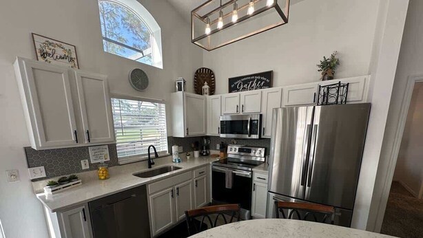 A modern kitchen with white cabinets, stainless steel appliances, and a large island. - Stay Awhile at the Fairways (Haines City)