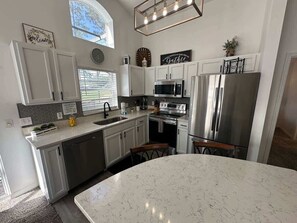 A modern kitchen with white cabinets, stainless steel appliances, and a large island. - Stay Awhile at the Fairways (Haines City)