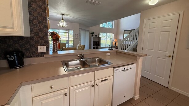 A kitchen with white cabinets, a stainless steel sink, a dishwasher, and a coffee maker. - The Solterra Sanctuary (Haines City)