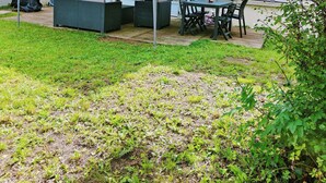 Un espace extérieur aménagé, abrité et doté d’une table et de chaises, entouré d’une pelouse et bordé d’un bâtiment avec des fenêtres.