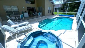 Una piscina con sillas de descanso y un jacuzzi, rodeada por un área de patio techada.
