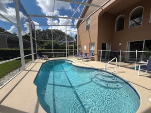 A swimming pool with a sunshade structure, lounge chairs, and a building with arched windows.