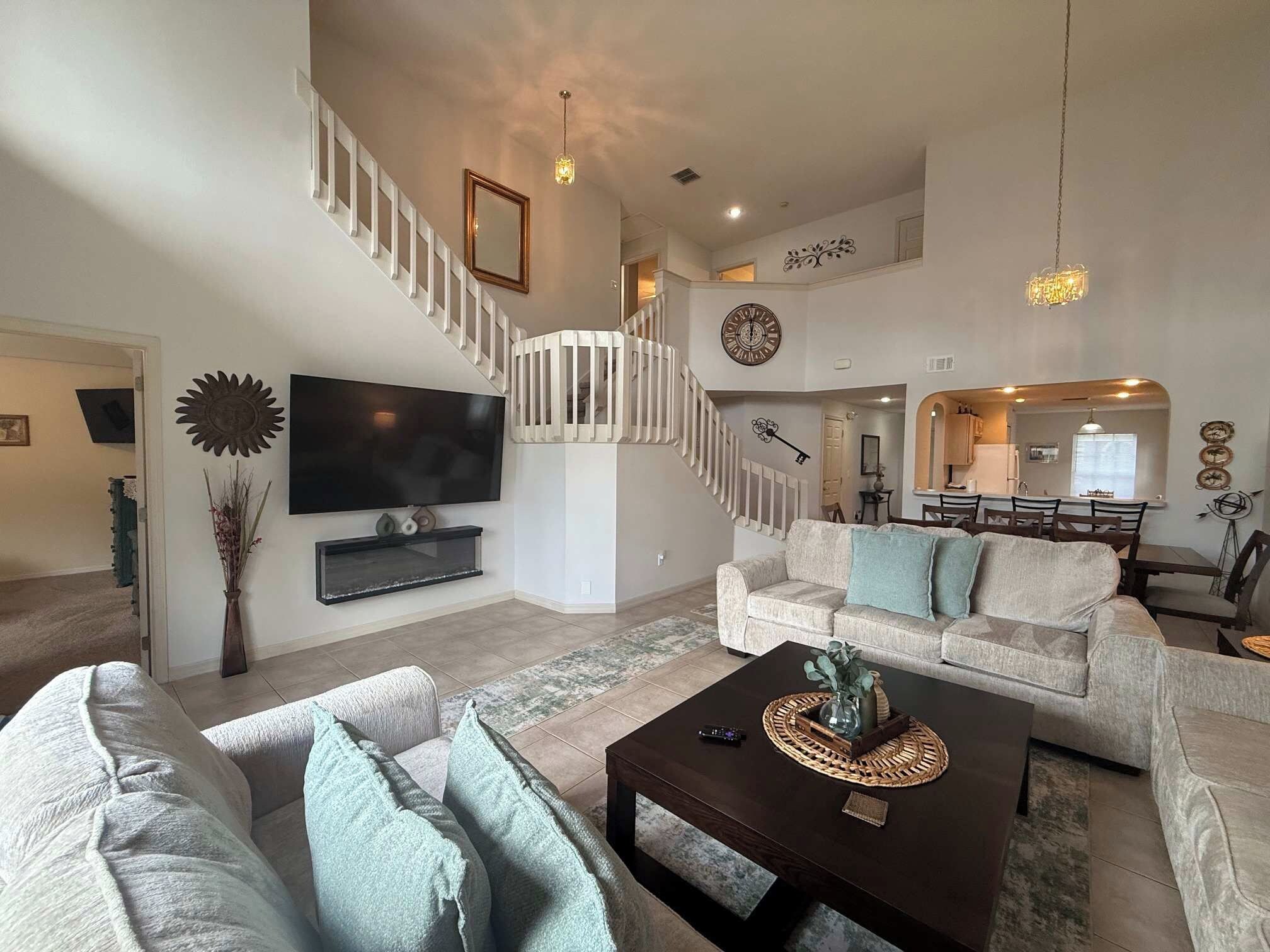 A spacious living room with a staircase, a flat-screen TV, a coffee table, and a sofa.