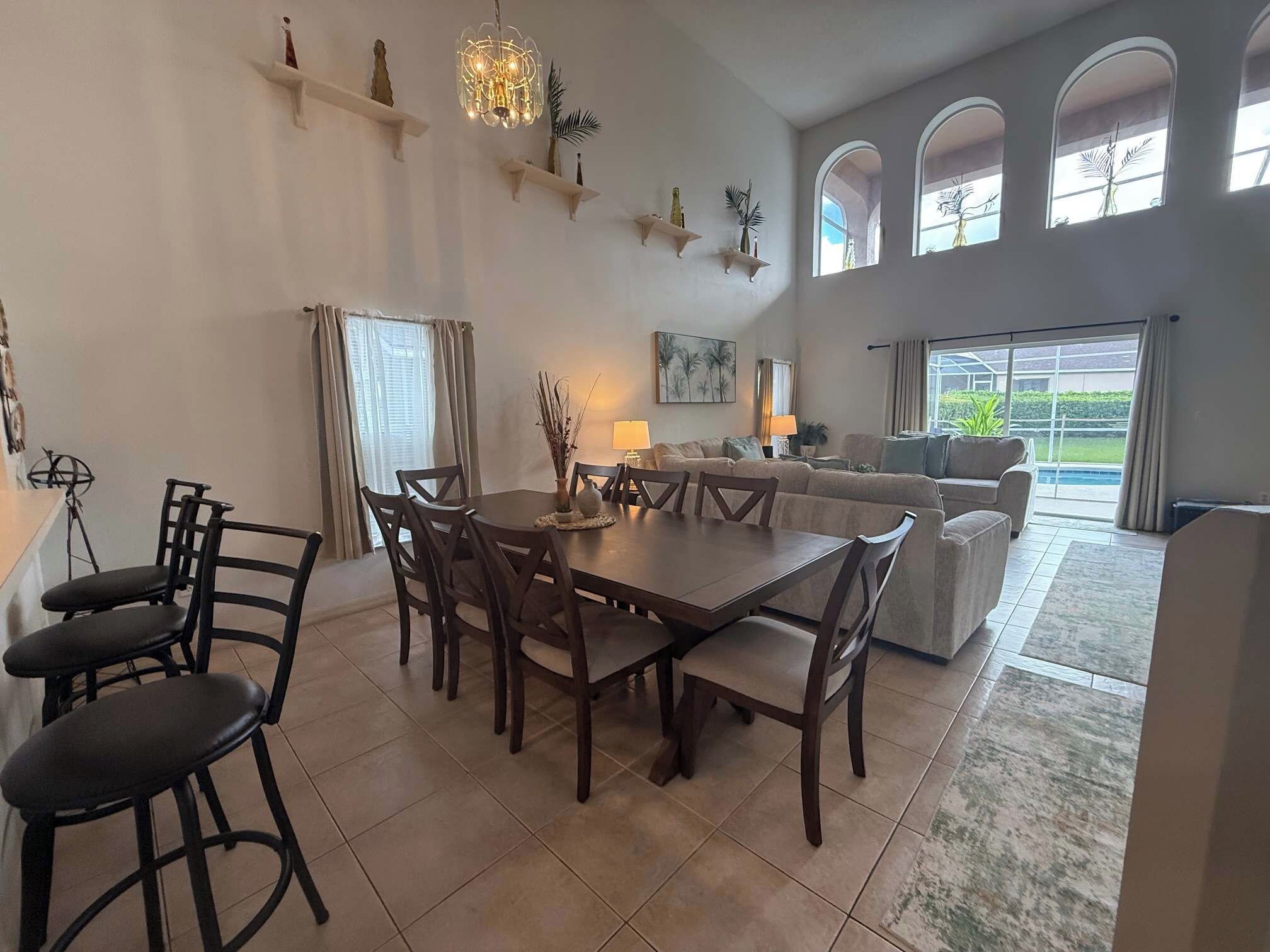 A spacious living area with a dining table, chairs, a sofa, and a large window with a view of greenery.