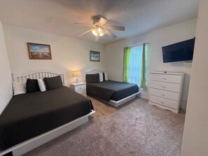 A bedroom with two beds, a ceiling fan, a dresser, and a TV mounted on the wall. - Golden Fairway Retreat (Haines City)