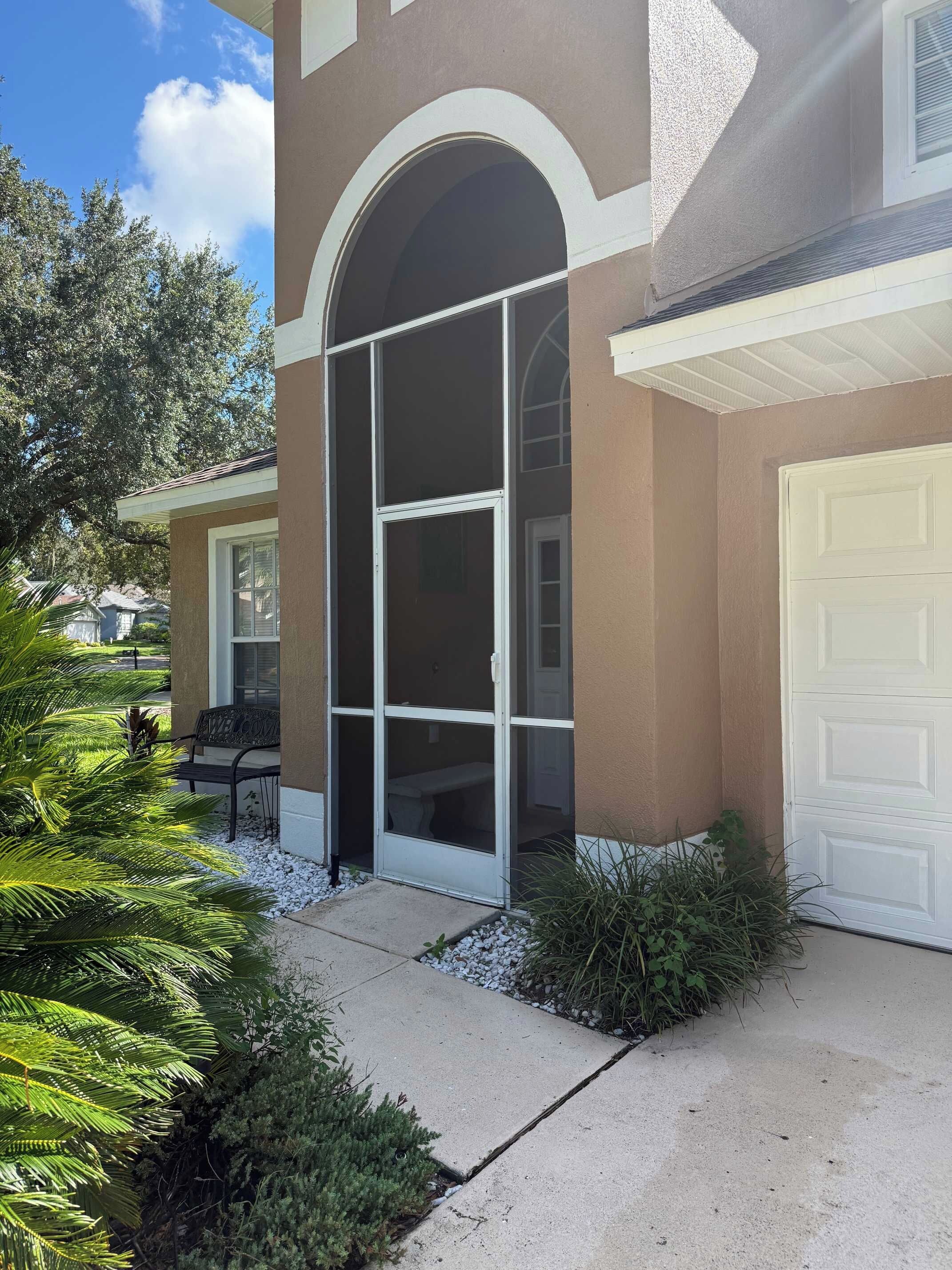 A residential building with a covered entryway, a garage door, and a patio area with plants.