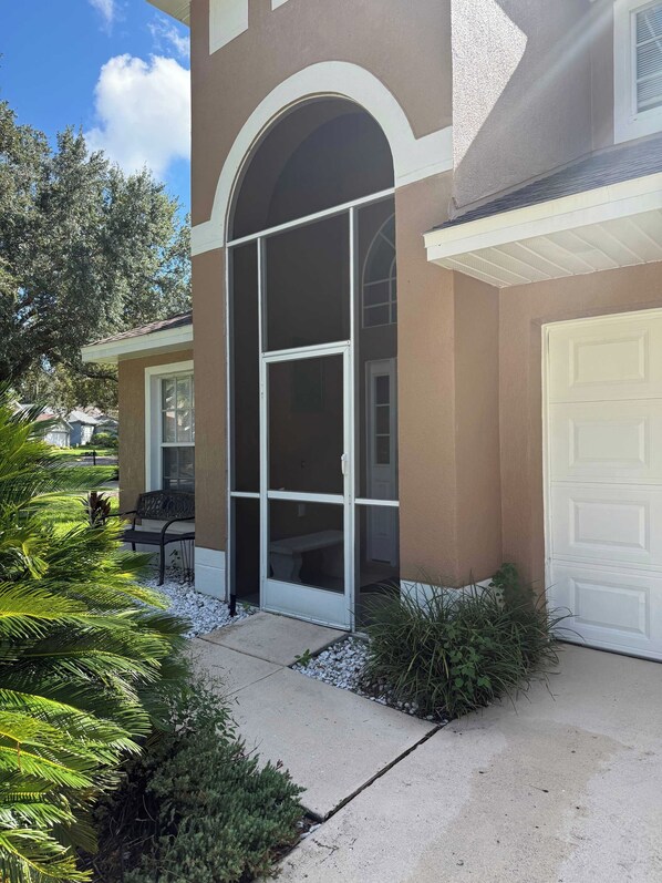 A residential building with a covered entryway, a garage door, and a patio area with plants.