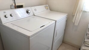 Ein kleiner Waschraum mit einer Waschmaschine und einem Trockner mit Frontlader, ein kleines Regal mit Pflegeprodukten und ein Metallgestell mit gefalteten Handtüchern.