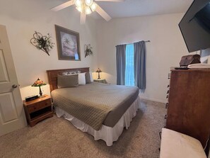 A bedroom with a bed, a nightstand, a lamp, a television, and a dresser.