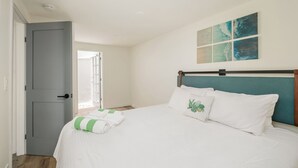 A bedroom with a bed, a grey door, and a window with blinds. - First Floor King Suite (101) (Oceanside)