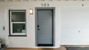 A house number 103, a grey door, a white garage door, and a window with blinds. - First Floor King Suite (101) (Oceanside)