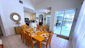 A dining area with a wooden table and chairs, a kitchen in the background, and a sliding glass door leading to an outdoor area. - Championship View Villa (Haines City)