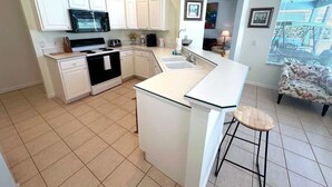 A compact kitchen with white cabinets, a black microwave, and a small island with a sink. - Championship View Villa (Haines City)