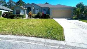 A residential house with a garage, a well-maintained lawn, and a clear sky. - Championship View Villa (Haines City)